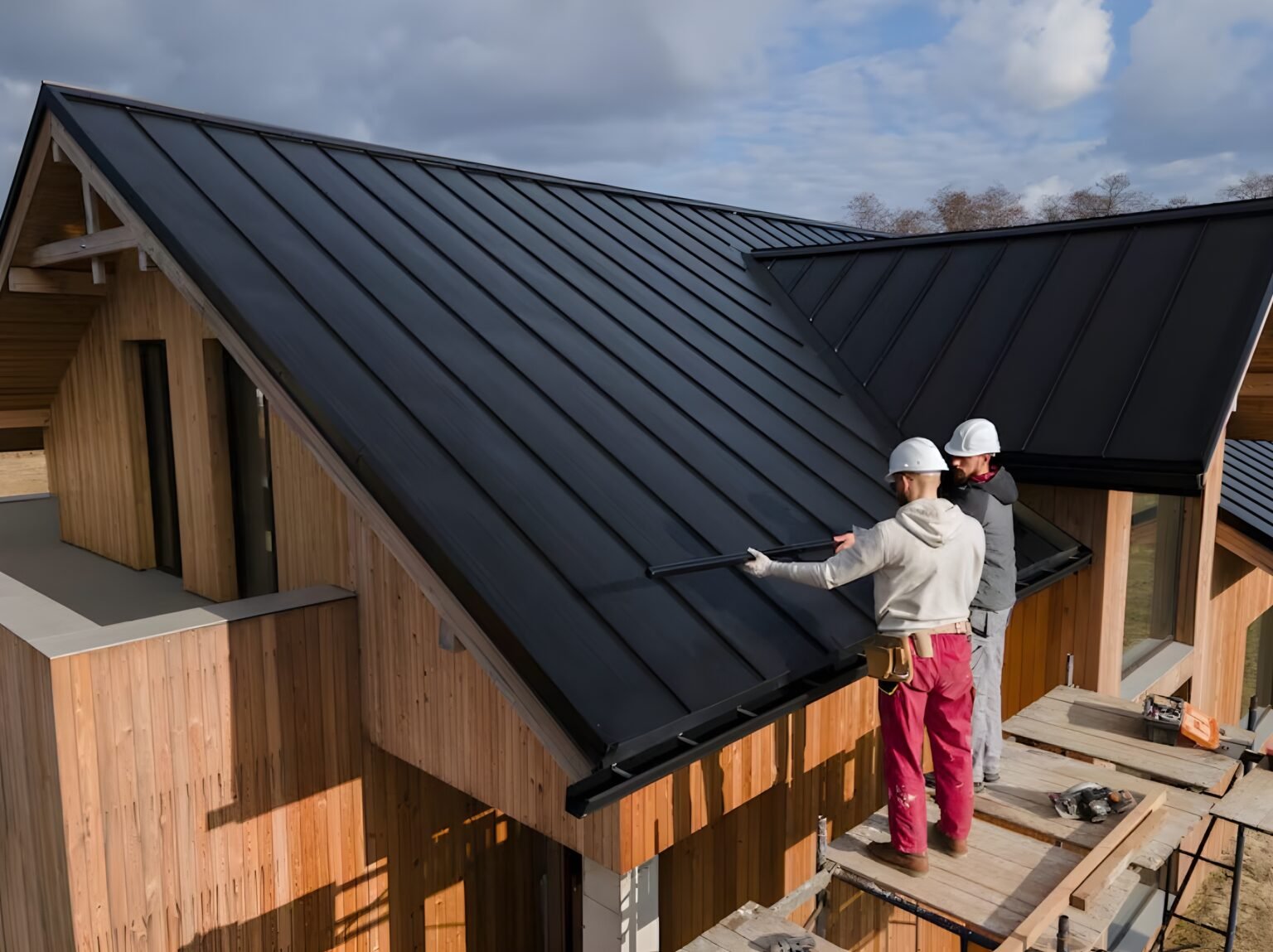 Roofing contractors installing sleek black standing seam metal roofing panels on a modern wooden home. Roof inspection in Bluffton.