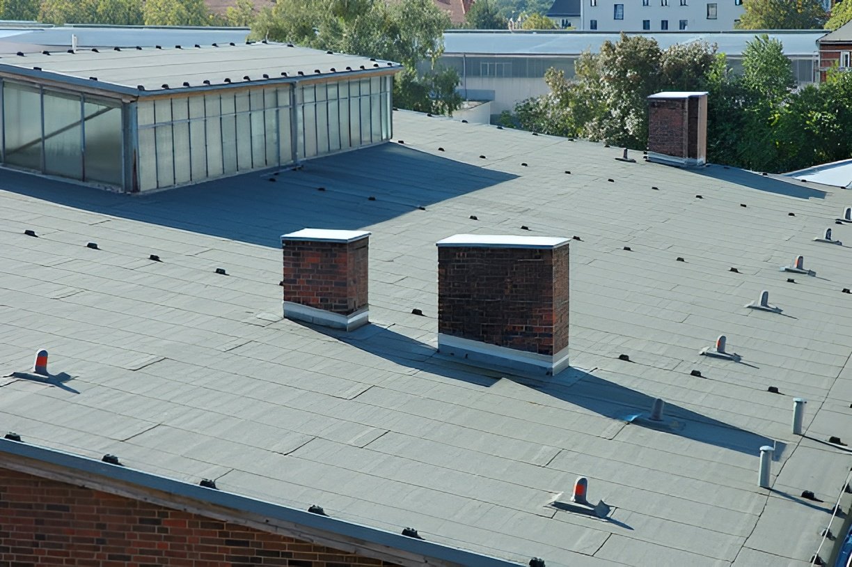 Commercial flat roof with asphalt membrane and multiple brick chimneys surrounded by urban buildings. Flat roofing services in Bluffton. Flat roofing services in Hilton Head Island