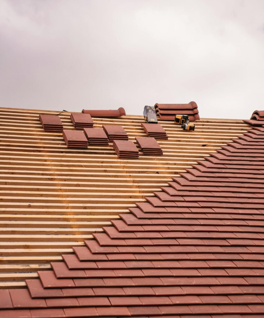 Partially completed roof installation showing red clay tiles being laid over wooden battens during construction. Tile roofing in Bluffton