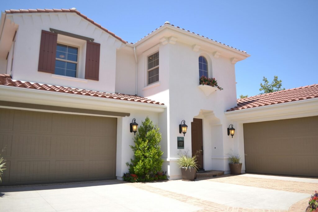 Two-story Mediterranean-style home with red clay tile roofing and white stucco exterior featuring a double garage and decorative window planter