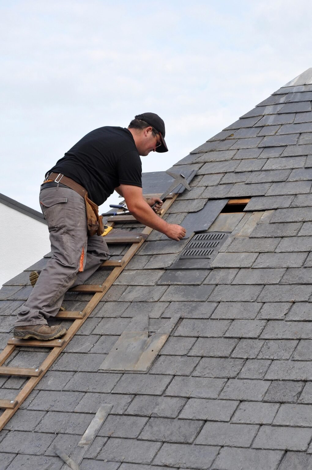 Roofer repairing and replacing shingles on a steep residential roof during maintenance work