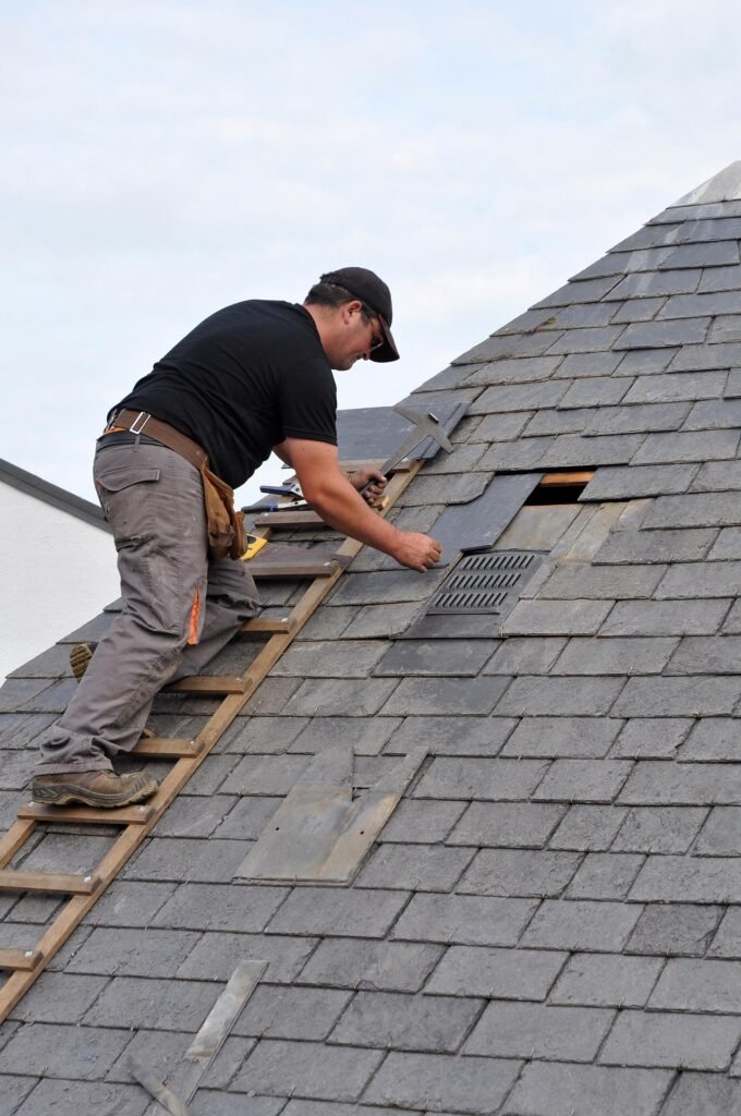 Roofer repairing and replacing shingles on a steep residential roof during maintenance work